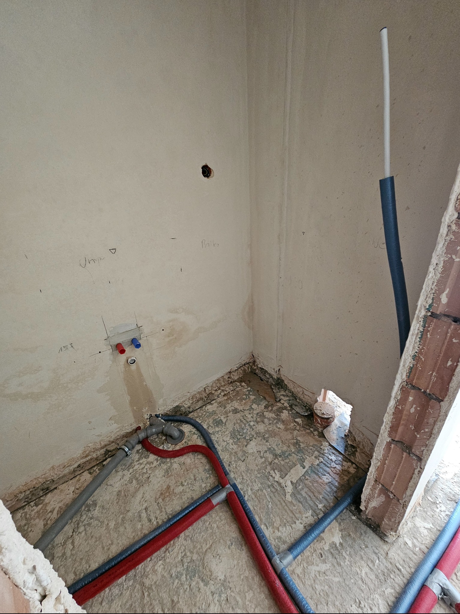 Fragment wnętrza w trakcie remontu z widoczną instalacją hydrauliczną: rury w izolacji w kolorach szarym i czerwonym, wystające ze ściany.