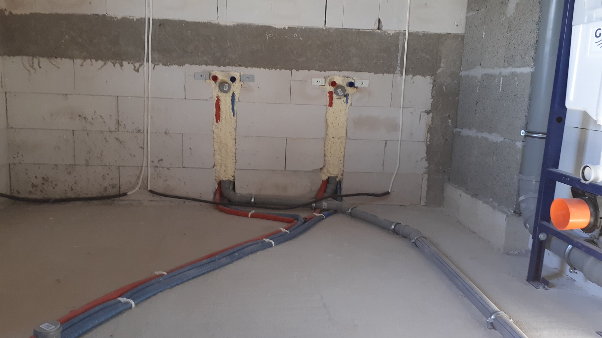 Wewnętrzne rury wodne i kanalizacyjne w trakcie montażu w surowym wnętrzu, ściany z betonu komórkowego, przewody z izolacją piankową.