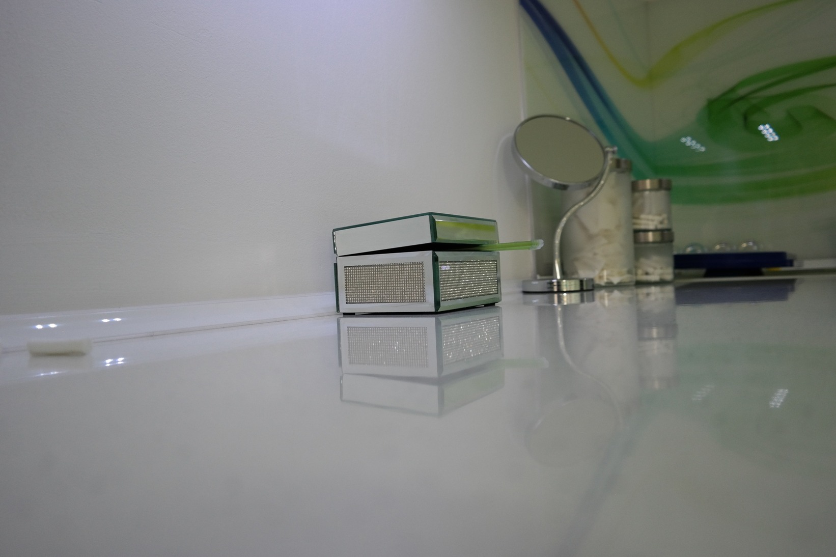 Błyszczące pudełko na akcesoria dentystyczne z zieloną szczoteczką, lusterko kosmetyczne i pojemniki na waciki na białym, lśniącym blacie w gabinecie.