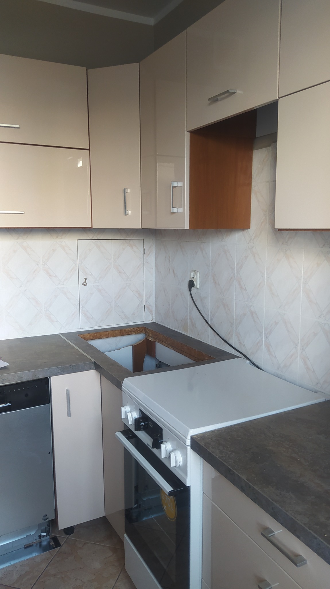 Montaż zlewu w kuchni z beżowymi, lakierowanymi szafkami i płytkami w romby na ścianie, widoczny otwór w blacie i fragment kuchenki.