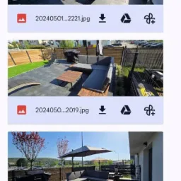 Umeblowany taras z szarej kostki brukowej z sofą narożną, stolikiem kawowym i parasolem. W tle widoczne drzewa i budynki. Całość w słoneczny dzień.