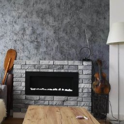 MARCUS Usługi Remontowe Marek Frydrychowski - Szara ściana z efektem betonu i elektryczny kominek obudowany cegłą. Drewniany stół i skrzypce w rogu tworzą przytulne wnętrze.
