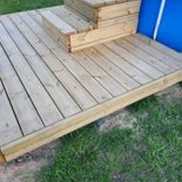 MARCUS Usługi Remontowe Marek Frydrychowski - Drewniany taras z dwustopniowymi schodkami przy basenie ogrodowym, widok z góry na jasne deski i zieloną trawę w tle. Świeżo zaimpregnowane drewno.