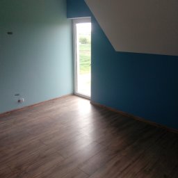 MARCUS Usługi Remontowe Marek Frydrychowski - Pokój po remoncie: ciemne panele, ściany pomalowane na dwa kolory (błękit i granat), białe okno z widokiem na zieleń. Widoczne gniazdka elektryczne i fragment poddasza.