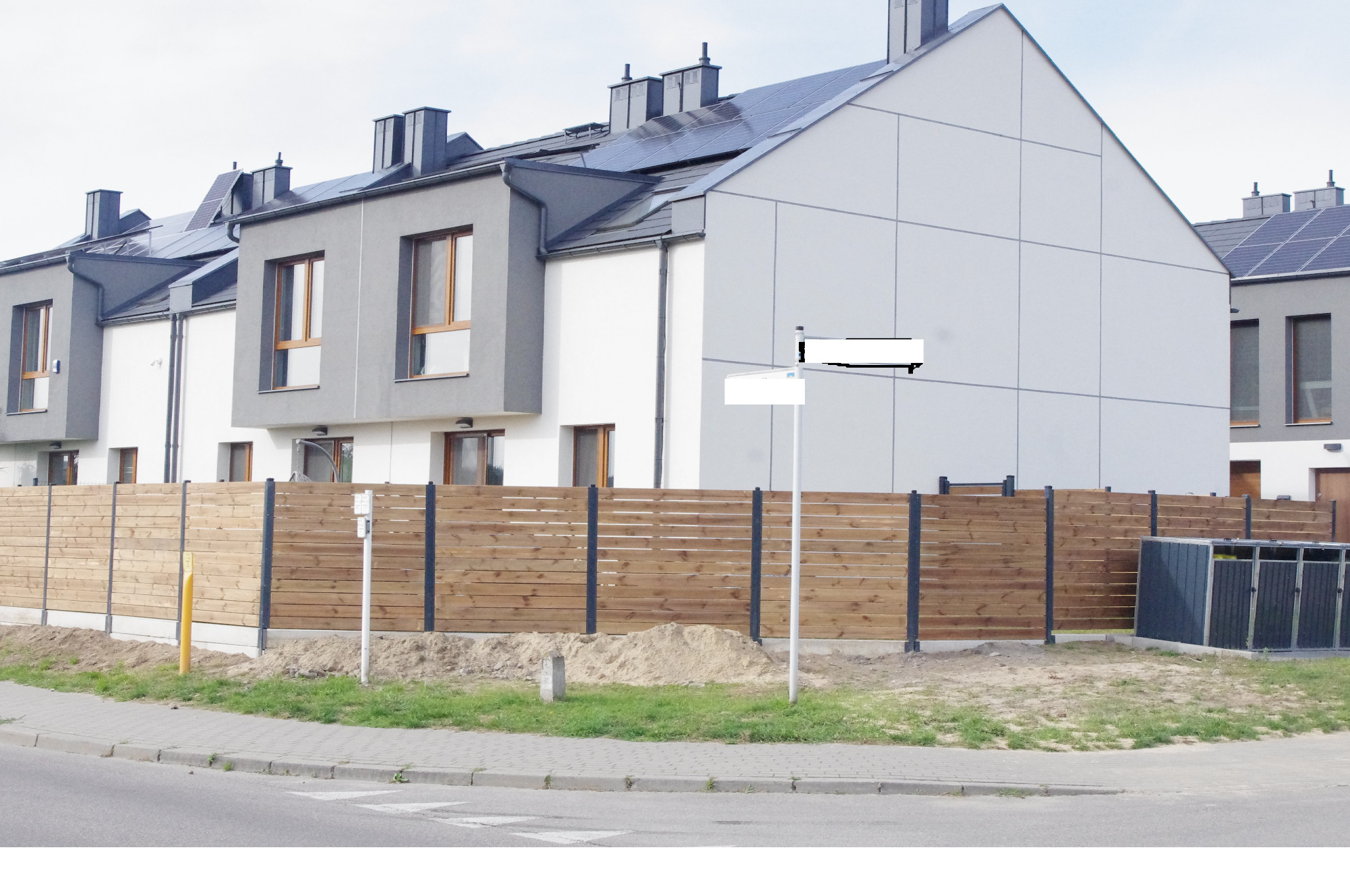 Nowoczesne segmenty mieszkalne z panelami słonecznymi i drewnianym ogrodzeniem z metalowymi słupkami. Widok z ulicy.
