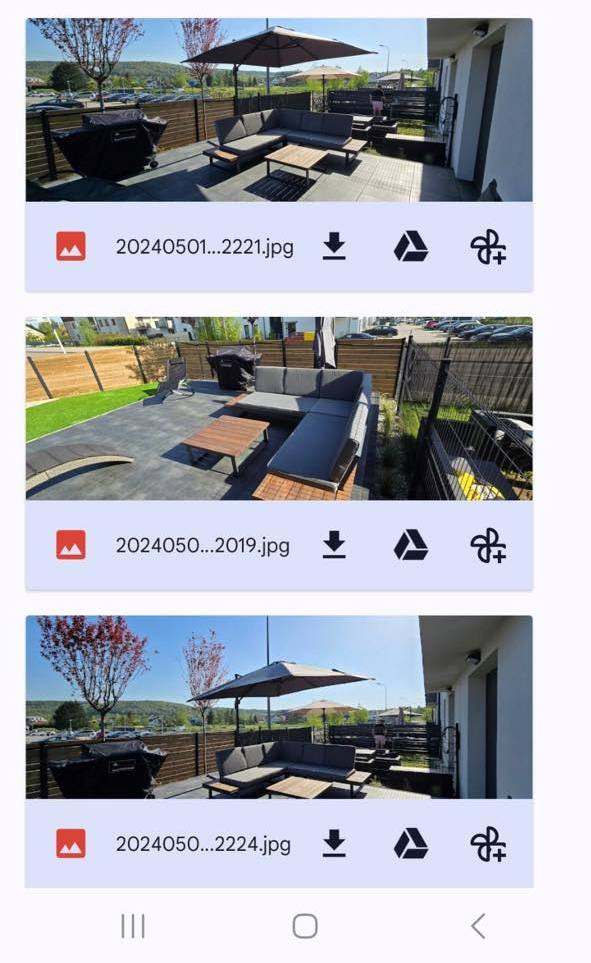 Umeblowany taras z szarej kostki brukowej z sofą narożną, stolikiem kawowym i parasolem. W tle widoczne drzewa i budynki. Całość w słoneczny dzień.