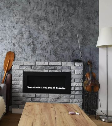 Szara ściana z efektem betonu i elektryczny kominek obudowany cegłą. Drewniany stół i skrzypce w rogu tworzą przytulne wnętrze.