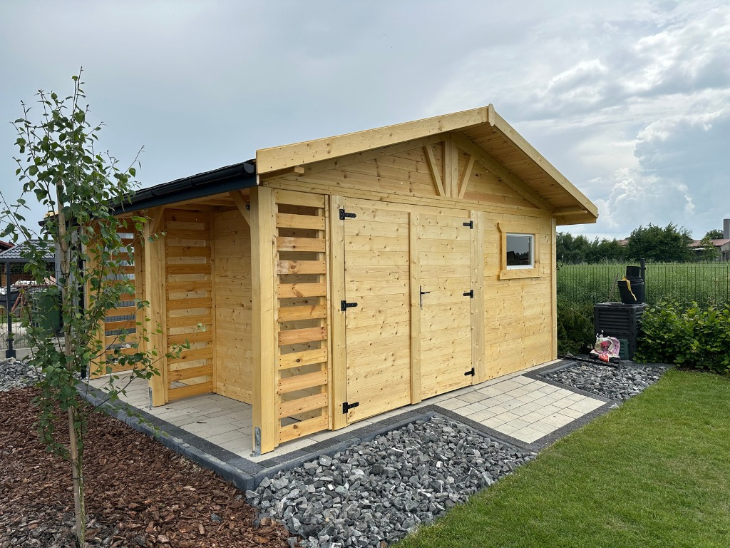 Drewniana altana z dwoma skrzydłami drzwiowymi i małym oknem, zadaszona weranda, otoczona kamieniami i trawnikiem, w tle zieleń i pochmurne niebo.