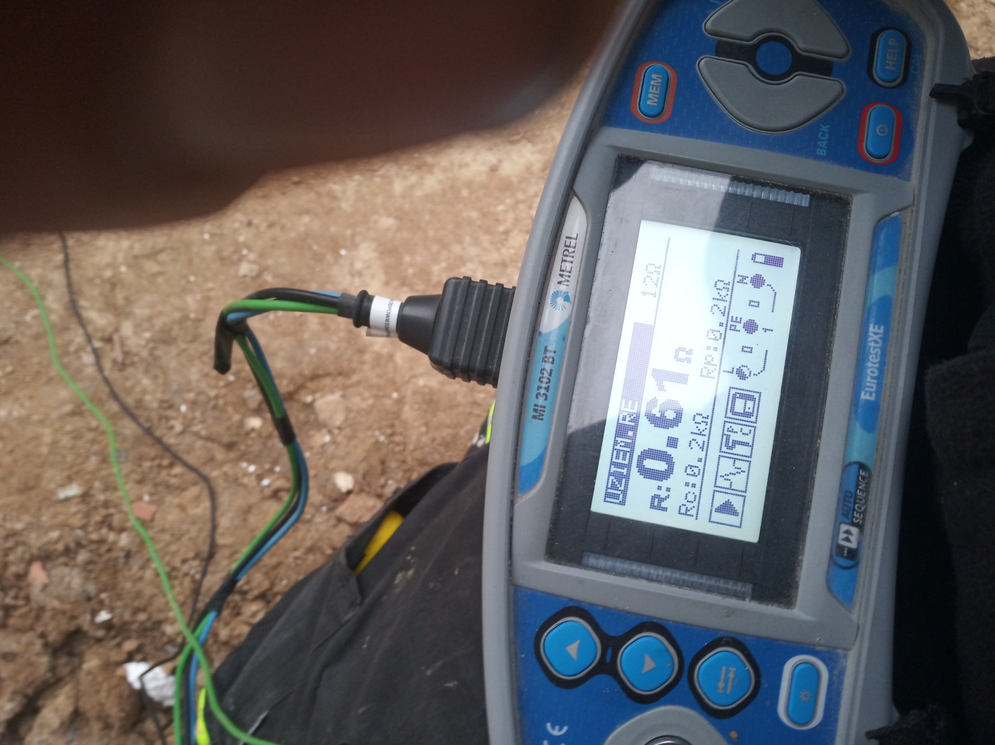 Miernik Metrel EurotestXE MI 3102 BT wyświetlający wynik pomiaru rezystancji uziemienia, z podłączonymi przewodami pomiarowymi na tle ziemi i fragmentu ubrania