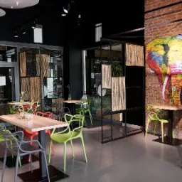 Wnętrze restauracji z kolorowymi krzesłami, drewnianymi stolikami i ścianą z motywem słonia, oddzielone bambusowymi parawanami.