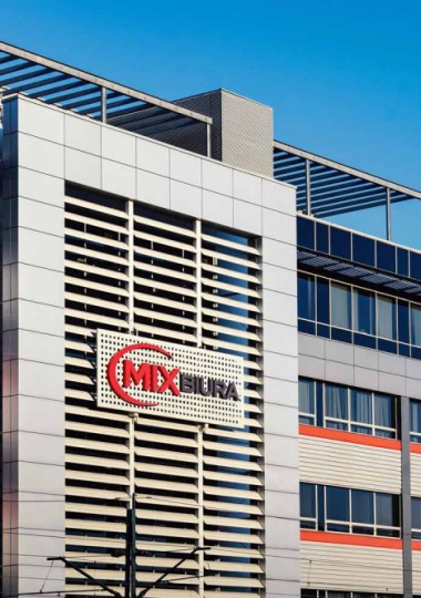 Nowoczesny budynek biurowy z logo 'MIX BIURA' na elewacji, widoczne okna i metalowe elementy architektoniczne na tle błękitnego nieba.