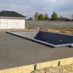 Wylany jastrych pod basen ogrodowy, widoczne szalunki i przygotowany nieckowy basen, w tle domek narzędziowy i mur z bloczków.