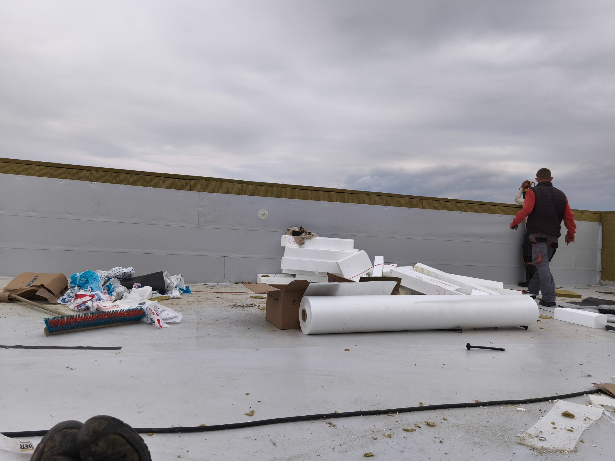 Prace dekarskie w Przytułach Stare: montaż izolacji na dachu z widocznymi materiałami izolacyjnymi i dekarzem w tle. Dach pokryty membraną.