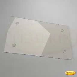 Prostokątna tafla szkła z czterema otworami, częściowo pokryta białą folią z geometrycznym wzorem, leżąca na szarym tle.