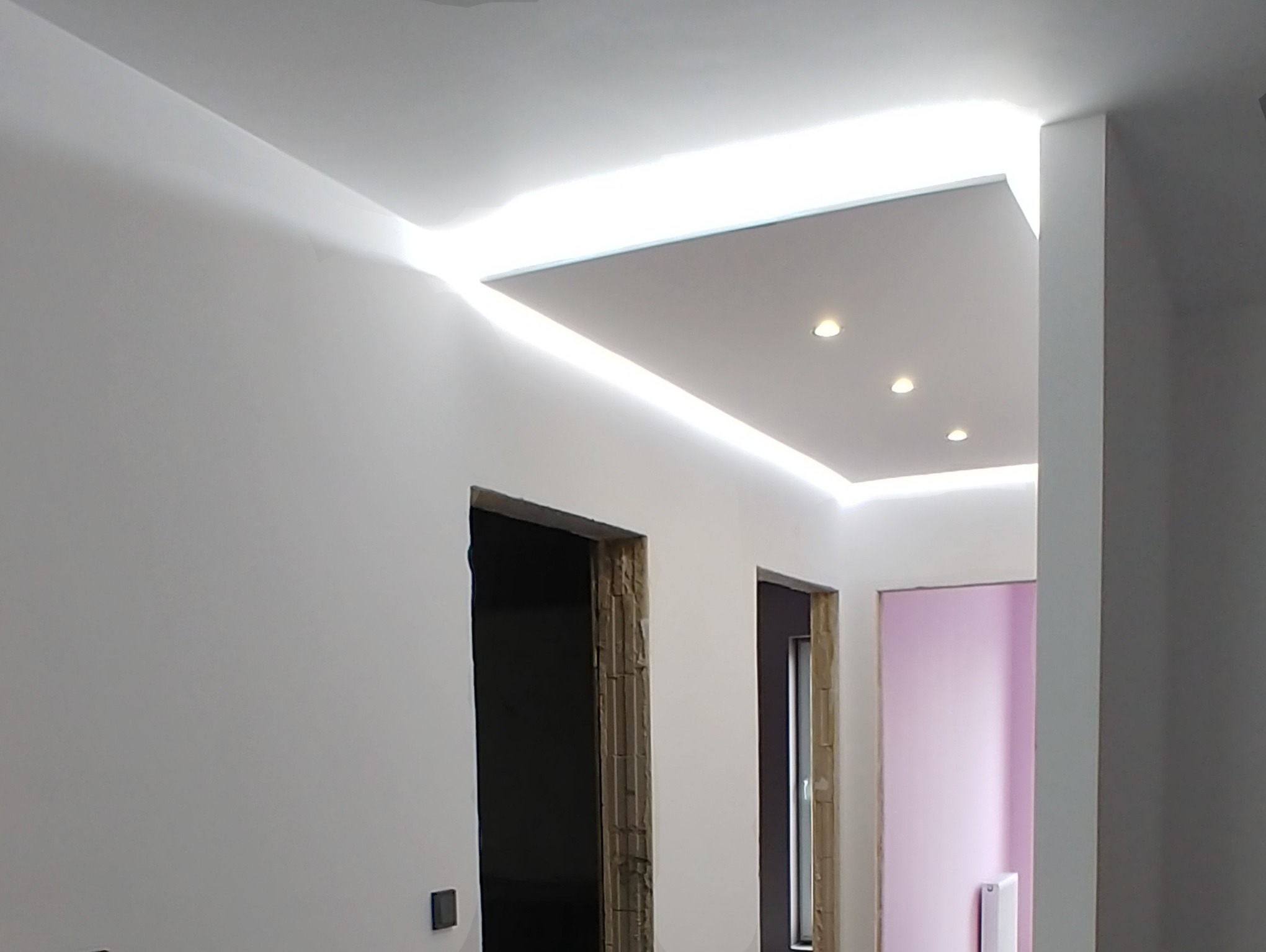 Nowoczesny sufit podwieszany z oświetleniem LED w korytarzu, widoczne przygotowane otwory na drzwi, ściany w kolorze białym.