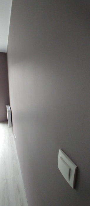 Świeżo pomalowana ściana w odcieniach fioletu z zamontowanym białym włącznikiem światła i widocznym grzejnikiem w tle, perspektywa z dołu.