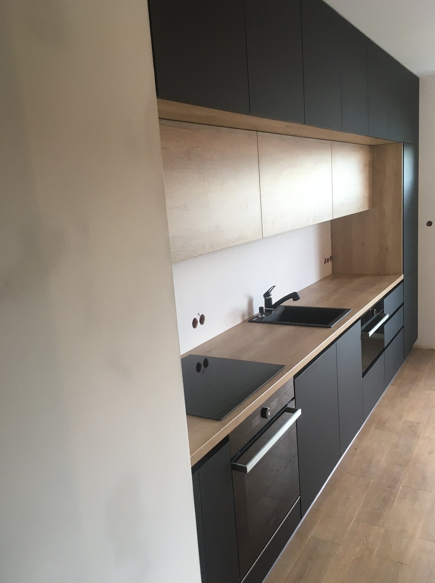 Nowoczesna kuchnia z czarnymi szafkami i drewnianym blatem w trakcie montażu w Krakowie, widoczne niedokończone ściany i podłączenia elektryczne.