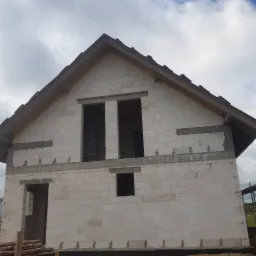 Niedokończony dom murowany z białych bloczków w Siedlcu, widoczne otwory okienne i drzwiowe, częściowo otynkowane nadproża i fundamenty, na pierwszym planie stos drewna.