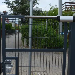 Szara metalowa brama wjazdowa z automatyką, widoczny panel z kodem, ulica w tle.