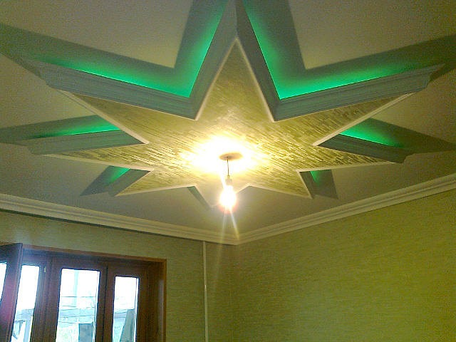 Dekoracyjny sufit z gipsowo-kartonową konstrukcją w kształcie gwiazdy, podświetlony zielonymi diodami LED, z centralnym oświetleniem żarówkowym i teksturowaną powierzchnią.