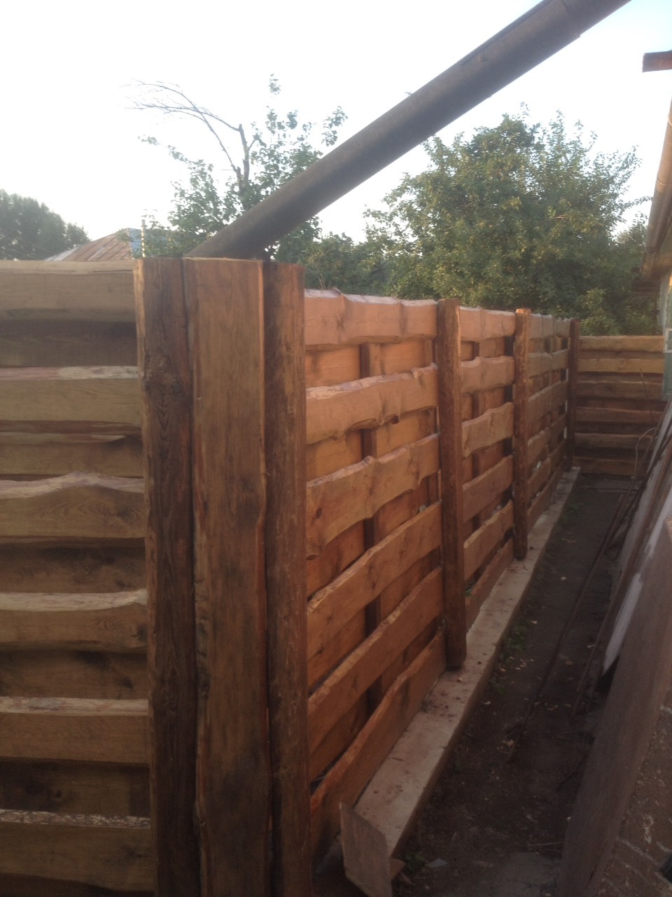 Nowo postawione, drewniane ogrodzenie z poziomych desek, zabezpieczone impregnatem, widok z dołu, z elementami konstrukcyjnymi w tle.