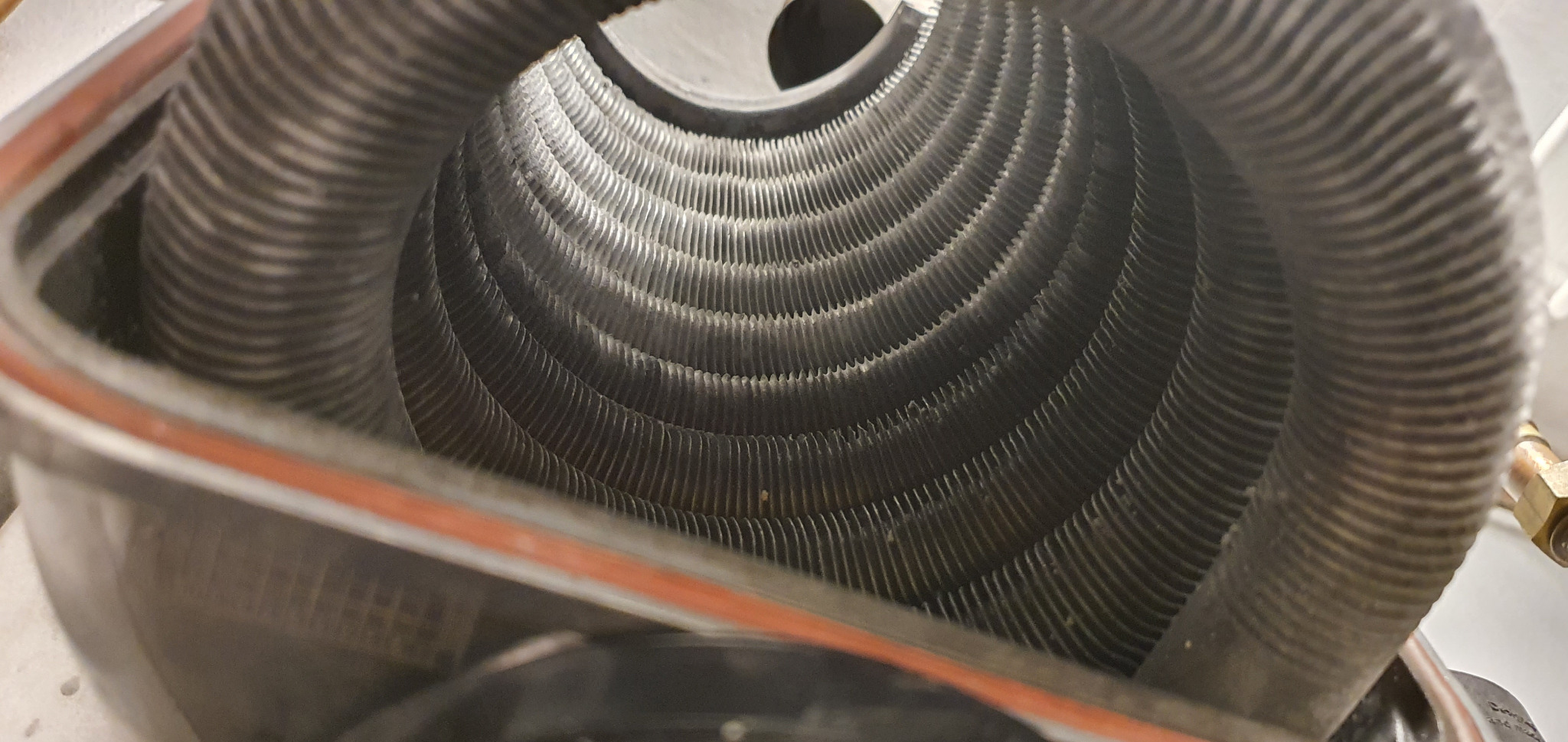 Wnętrze wymiennika ciepła z widocznymi rurkami z ożebrowaniem, element instalacji grzewczej, zarys obudowy z pomarańczową uszczelką.