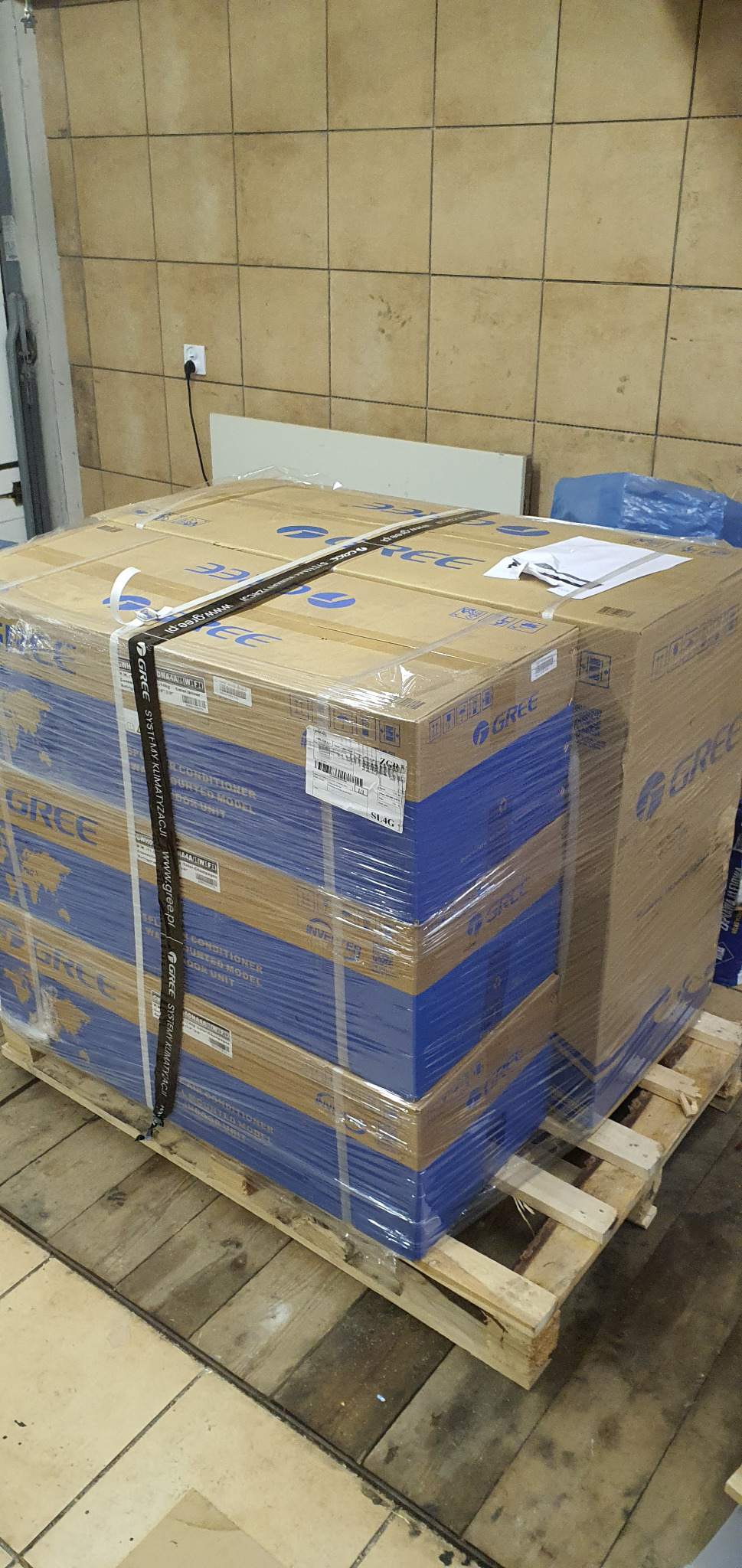 Paleta z zapakowanymi w folię i spiętymi taśmą kartonami klimatyzatorów marki Gree, widoczne etykiety i oznaczenia producenta.