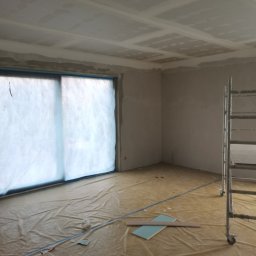 ReMalFach - Pokój w trakcie prac wykończeniowych: zabezpieczone okno folią, położona płyta karton gips na suficie, widoczne ślady szpachlowania na ścianach, rozłożona folia ochronna na podłodze.