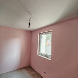 ReMalFach - Pokój po malowaniu na różowo z nowym oknem, widoczna wisząca żarówka i szare płytki na podłodze. Świeżo pomalowane ściany i sufit.