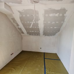 ReMalFach - Pokój na poddaszu w trakcie prac. Widoczne płyty karton-gips na suficie, wstępnie szpachlowane łączenia. Podłoga zabezpieczona folią ochronną. Ściany przygotowane do dalszych prac.