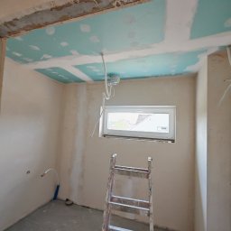 ReMalFach - Pokój w trakcie remontu: surowy strop, częściowo położona płyta karton-gips na suficie, ściany po szpachlowaniu, drabina malarska. Widoczne instalacje.