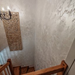ReMalFach - Ściana w odcieniach beżu z dekoracyjną strukturą, drewniana płaskorzeźba i schody z drewnianą balustradą. Widok z góry na wykończone wnętrze.