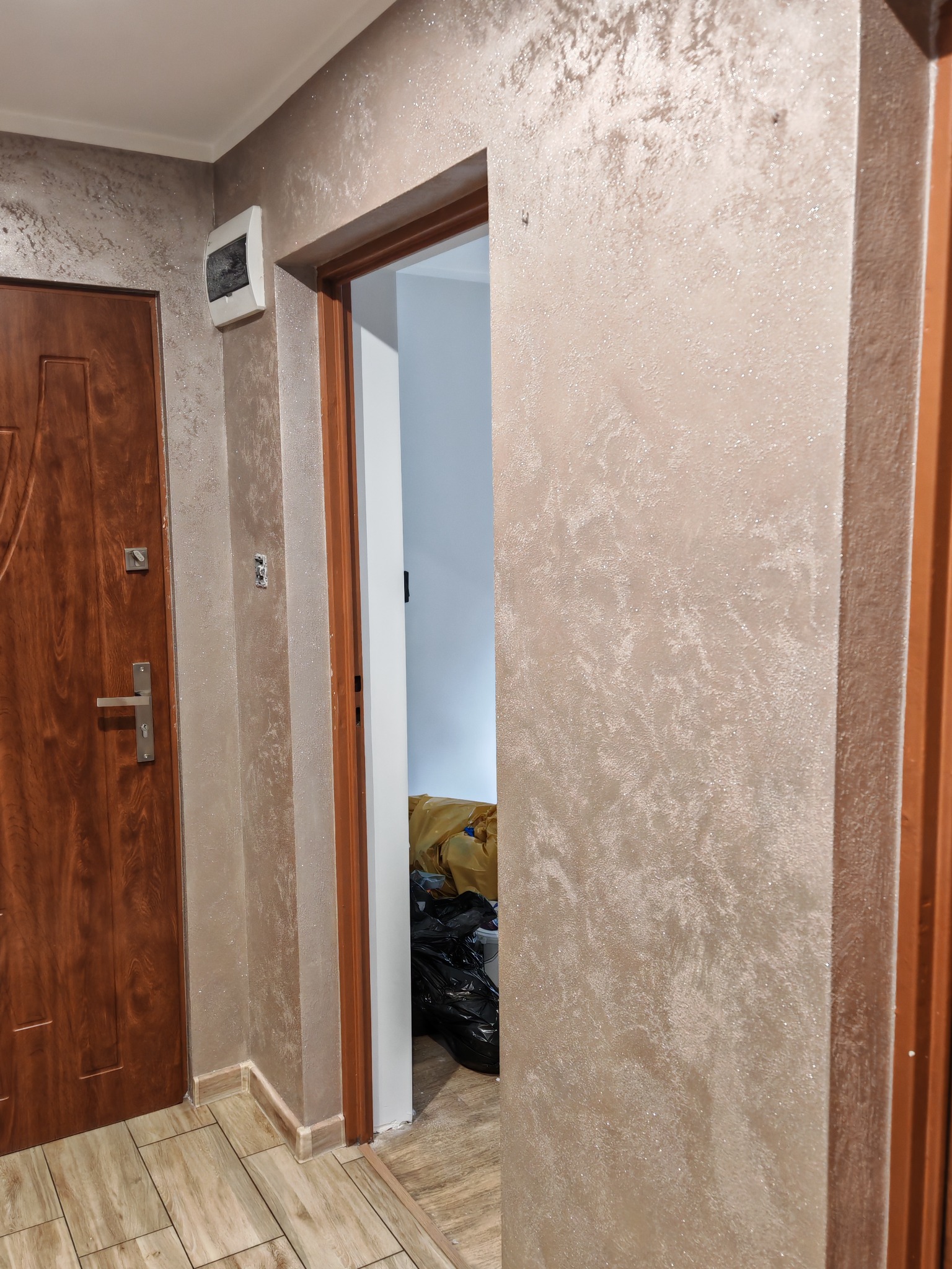 Korytarz po remoncie: drewniane drzwi wejściowe i wewnętrzne, ściany pokryte dekoracyjną, połyskującą farbą w odcieniach beżu i brązu, imitującą marmurkowy wzór.