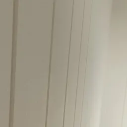 Ściana z pionowymi panelami pomalowana na jasny, neutralny kolor, widoczna pod kątem, z delikatną fakturą i subtelnym cieniowaniem.