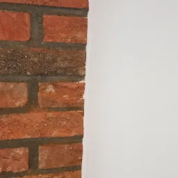 Fragment ściany z cegły klinkierowej sąsiadujący z gładką, pomalowaną na biało powierzchnią.