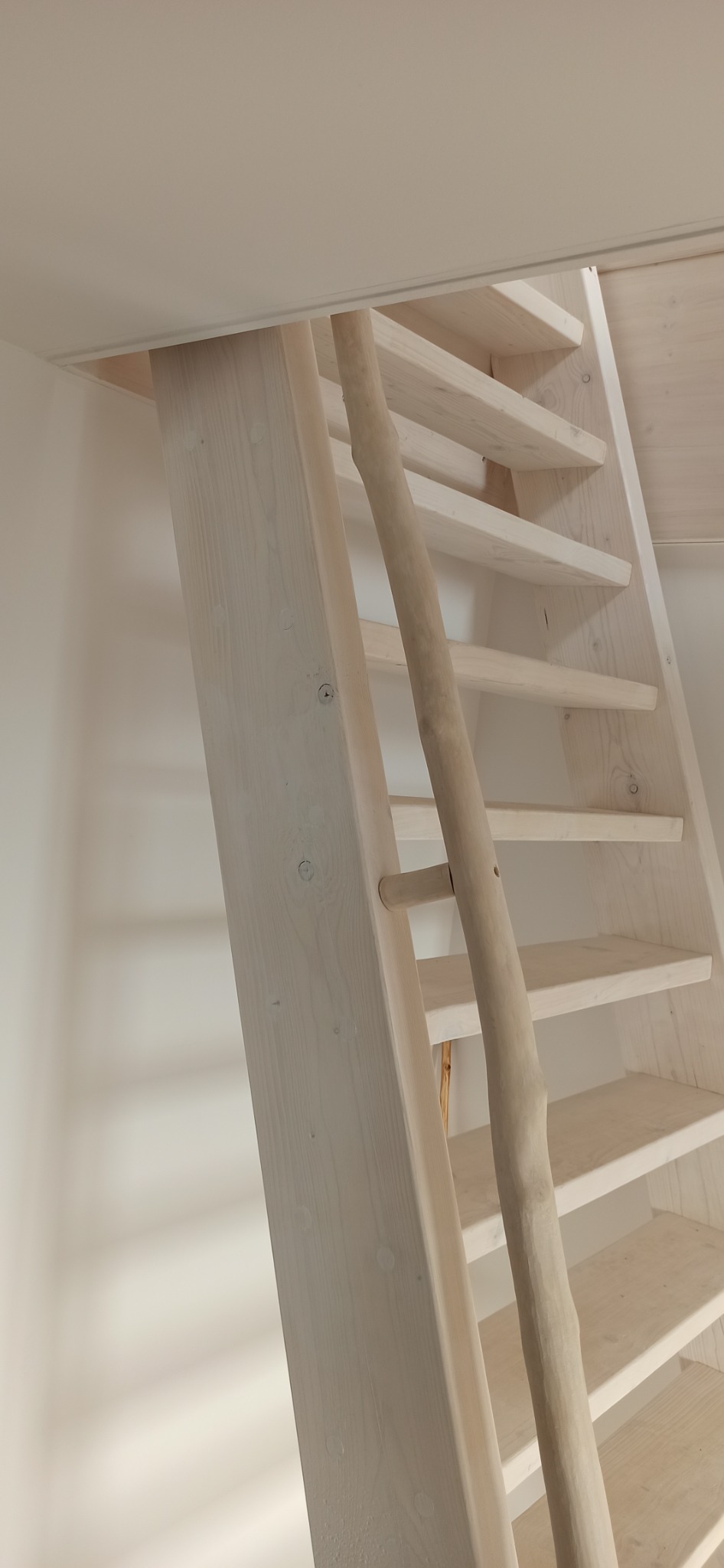 Białe drewniane schody strychowe z poręczą imitującą surowe drewno, widok z dołu.