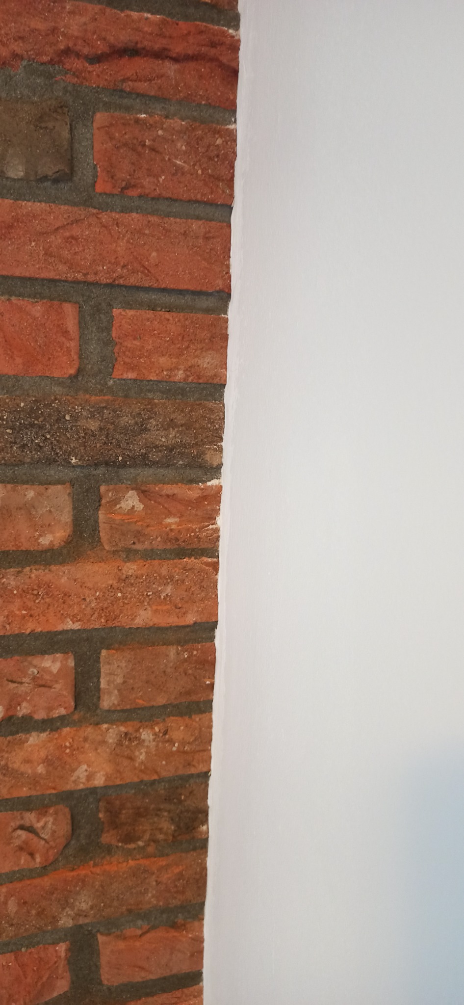 Fragment ściany z cegły klinkierowej sąsiadujący z gładką, pomalowaną na biało powierzchnią.