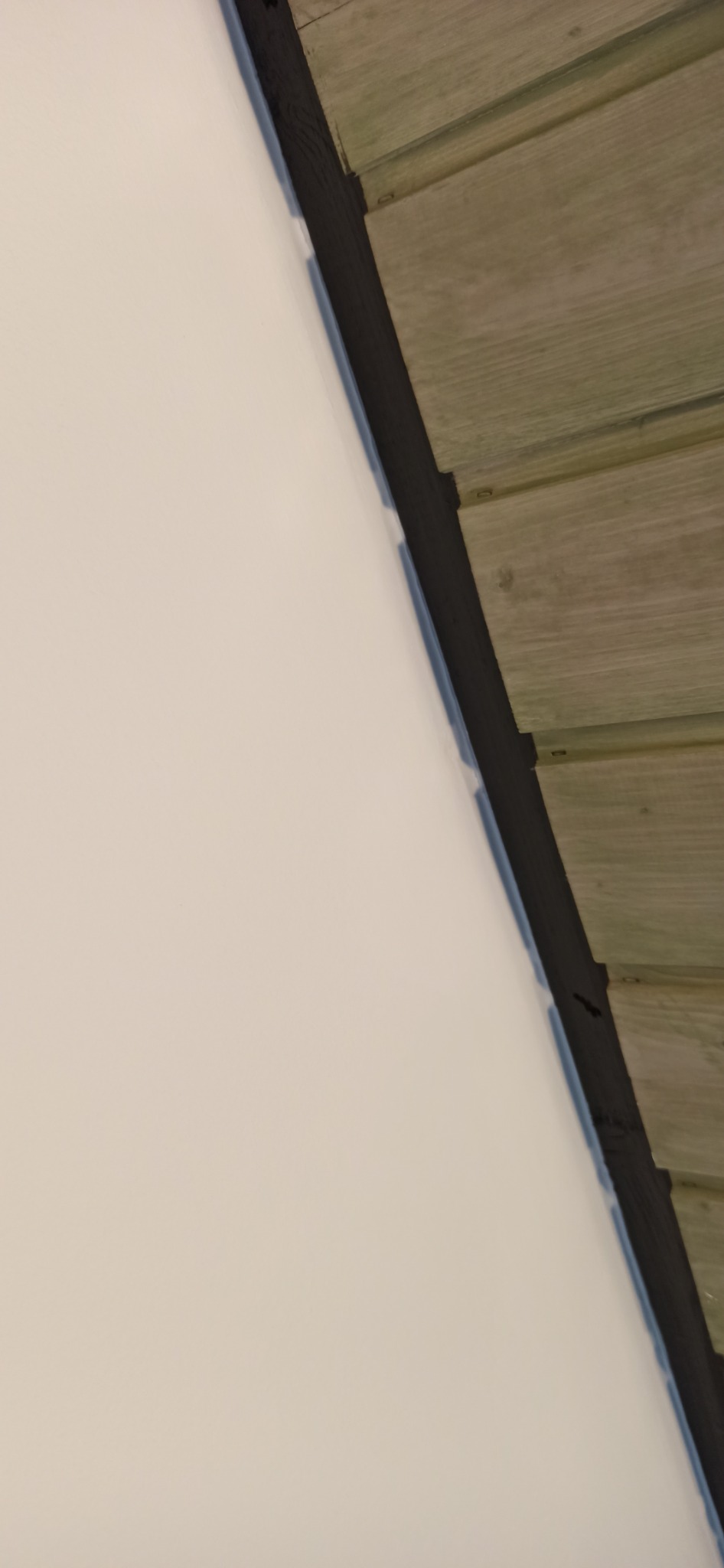 Fragment wykończonej ściany z gładzią i drewnianej boazerii oddzielonych czarną listwą dekoracyjną.