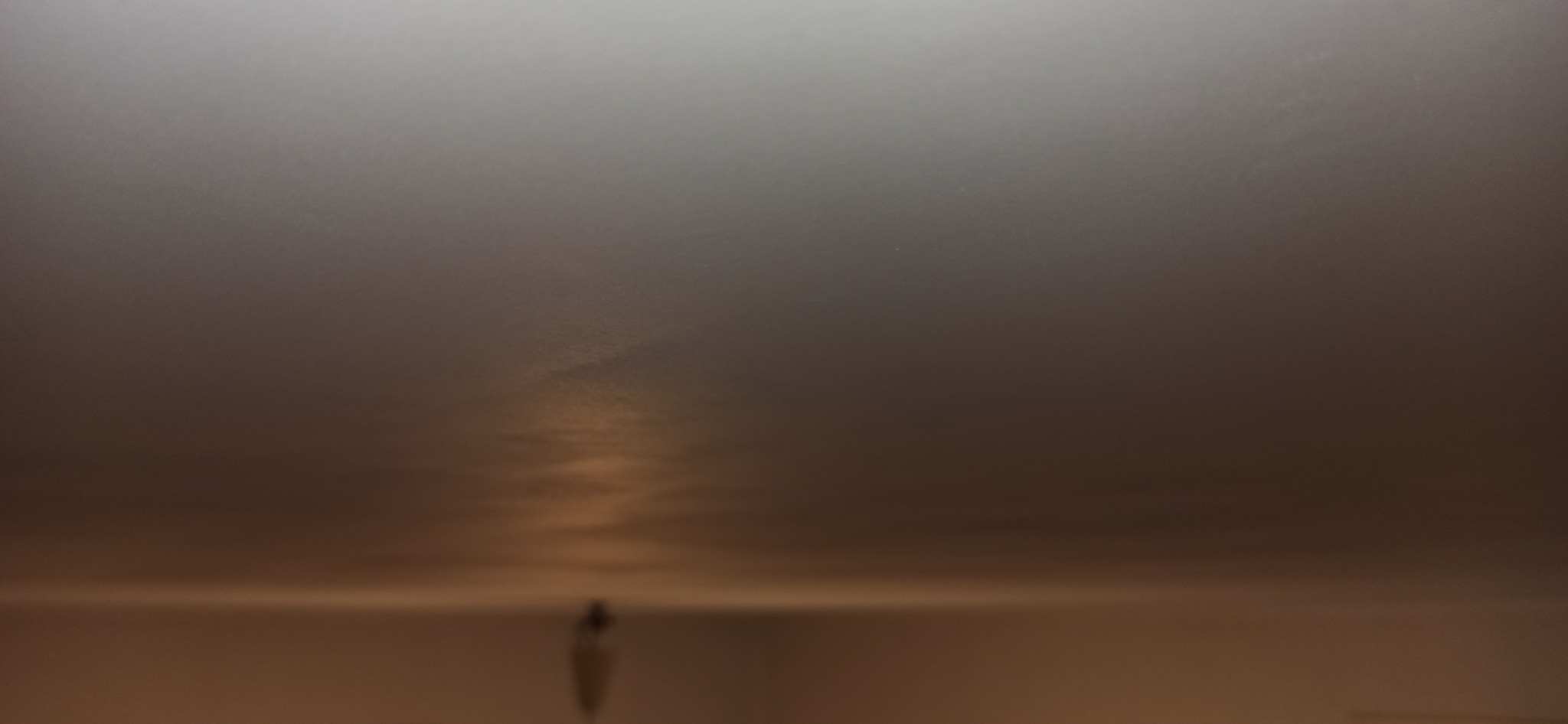 Nierównomiernie oświetlona, szara powierzchnia sufitu z widocznymi smugami i niedoskonałościami wykończenia.