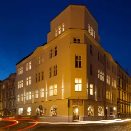 Odrestaurowana kamienica mieszkalna w Chorzowie oświetlona nocą, widoczne smugi świateł przejeżdżających samochodów na brukowanej ulicy.