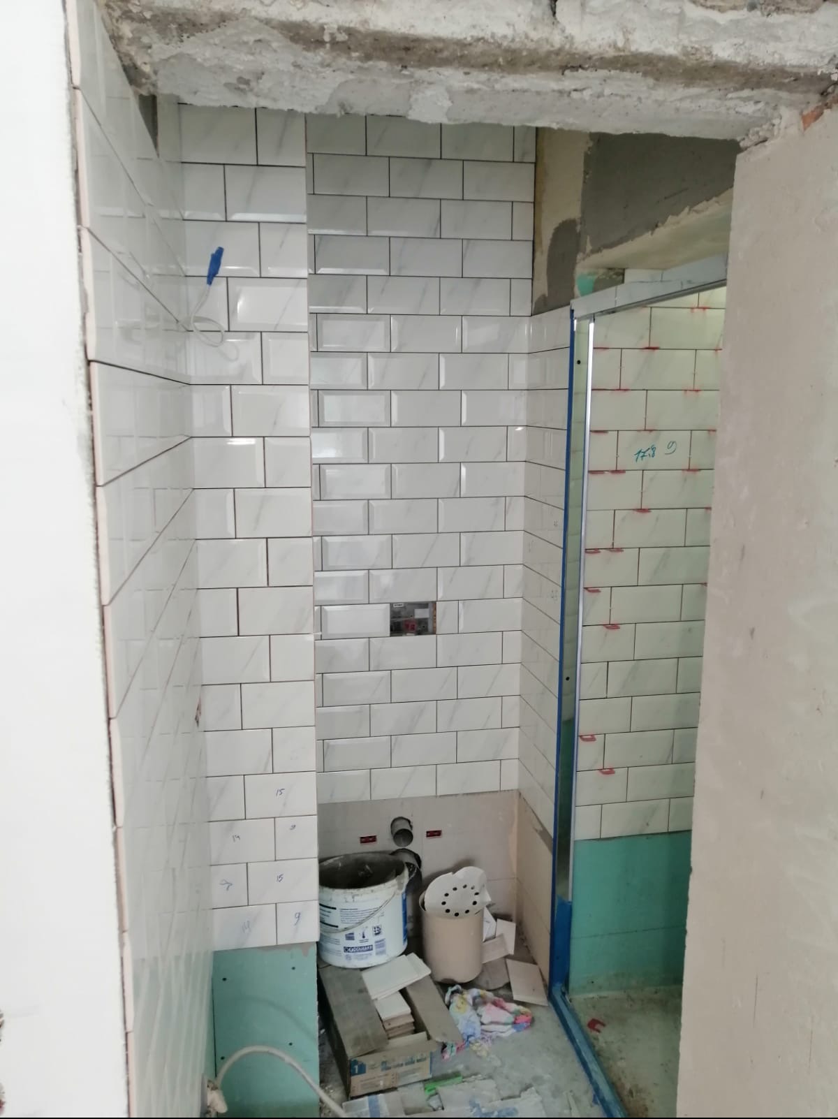 Układanie białych, prostokątnych płytek w łazience w trakcie remontu; widoczne narzędzia, wiadro z zaprawą i niedokończone fugowanie.