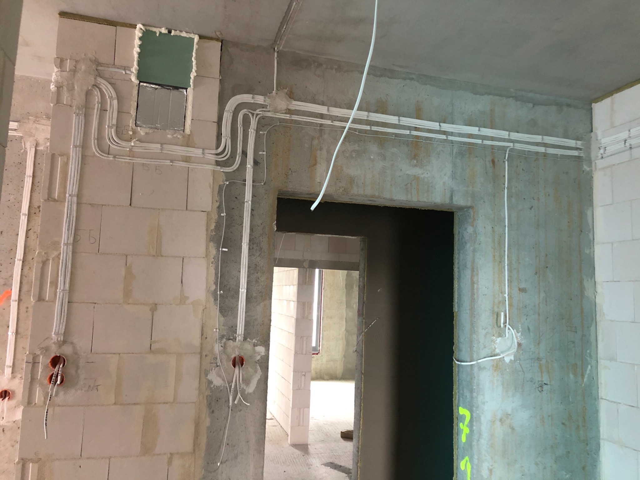 Instalacja elektryczna w surowym wnętrzu: białe kable prowadzone po ścianach z betonu komórkowego i betonowych, widoczne puszki instalacyjne, fragment okna w tle.