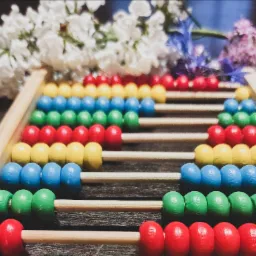Kolorowe liczydło z drewnianymi koralikami ułożone na drewnianym stole, z bukietem kwiatów w tle.
