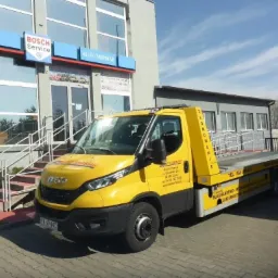 Żółta laweta Iveco firmy Auto Mirmar zaparkowana przed budynkiem z logo Bosch Service, widoczne numery telefonów i adres firmy na pojeździe.
