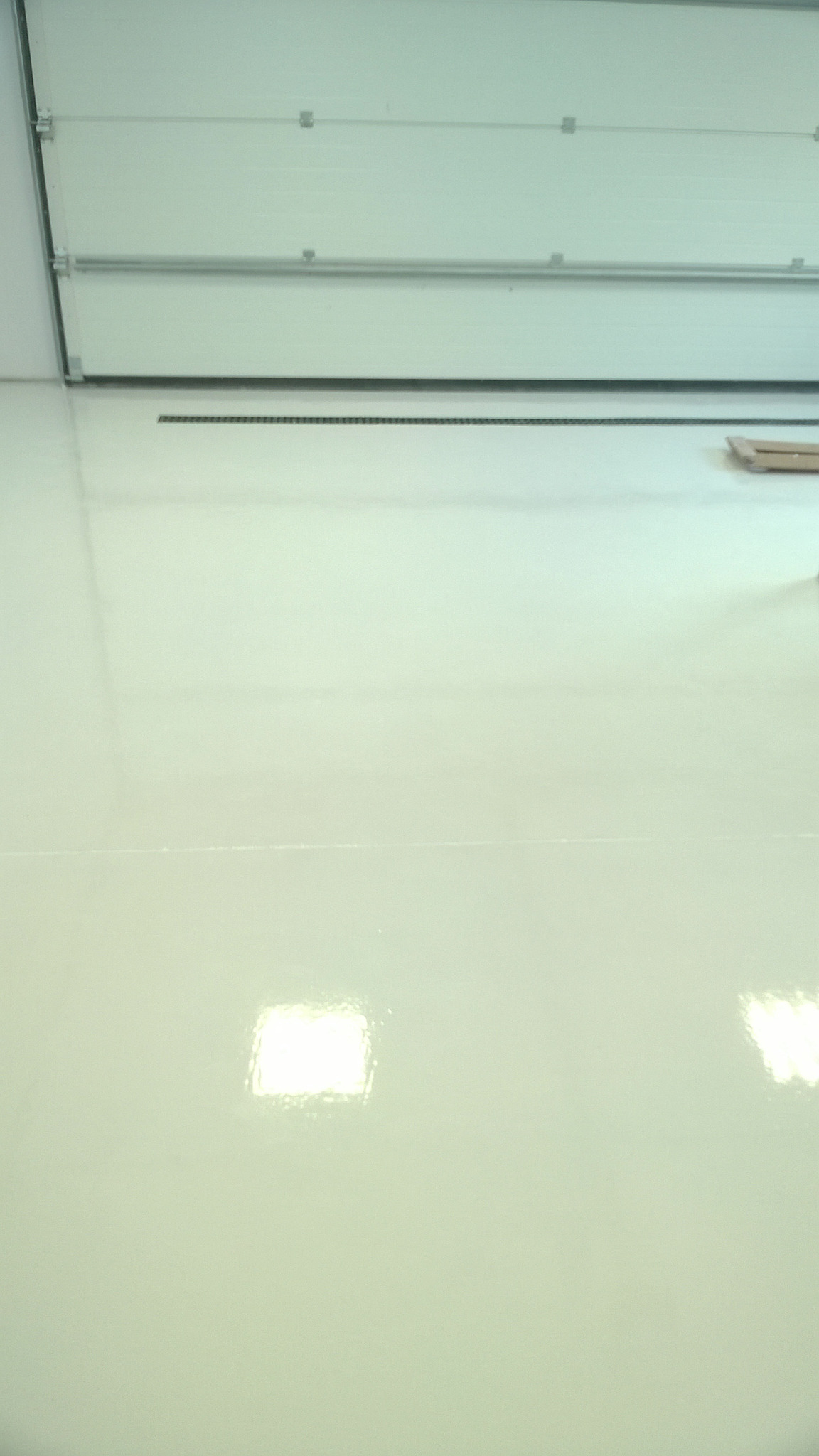 Błyszcząca, jasna podłoga w hali z widoczną bramą segmentową w tle.