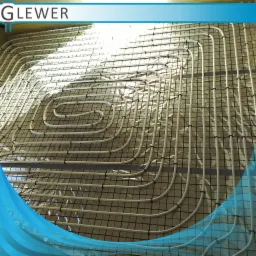 Białe rury układane w spiralny wzór na czarnej siatce, instalacja ogrzewania podłogowego na folii odblaskowej.