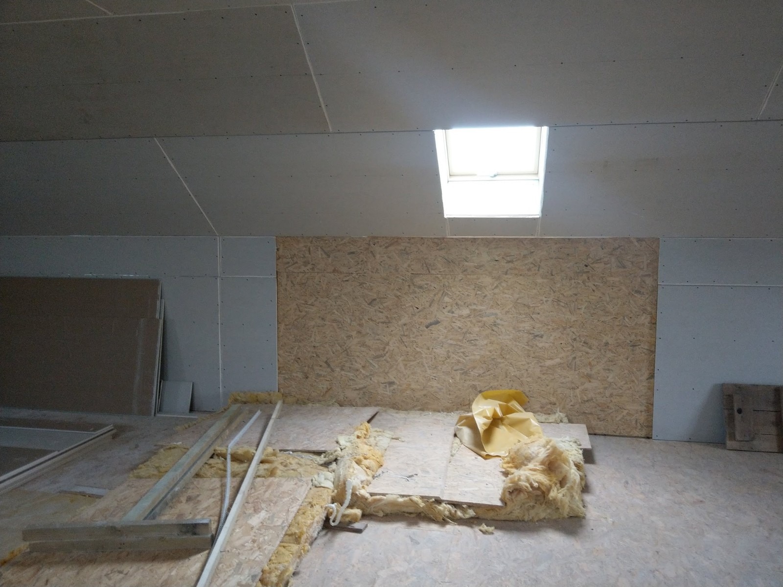 Poddasze w trakcie wykańczania: płyty OSB na ścianie, wełna mineralna na podłodze, sufit z płyt gipsowo-kartonowych z oknem dachowym.
