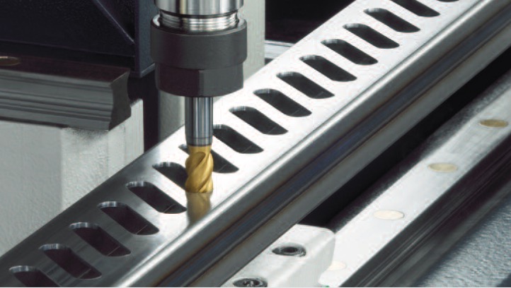 Frezarka CNC obrabiająca metalowy profil z podłużnymi otworami, widoczny złoty frez i metalowe prowadnice.