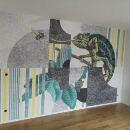 Wzorzysta tapeta przedstawiająca kameleona polującego na muchę, na ścianie w pokoju z drewnianą podłogą i grzejnikiem.