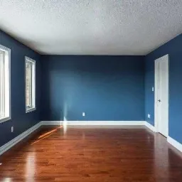 Pusty pokój z ciemnoniebieskimi ścianami, drewnianą podłogą i białymi listwami przypodłogowymi; na ścianie zamontowany uchwyt do telewizora.